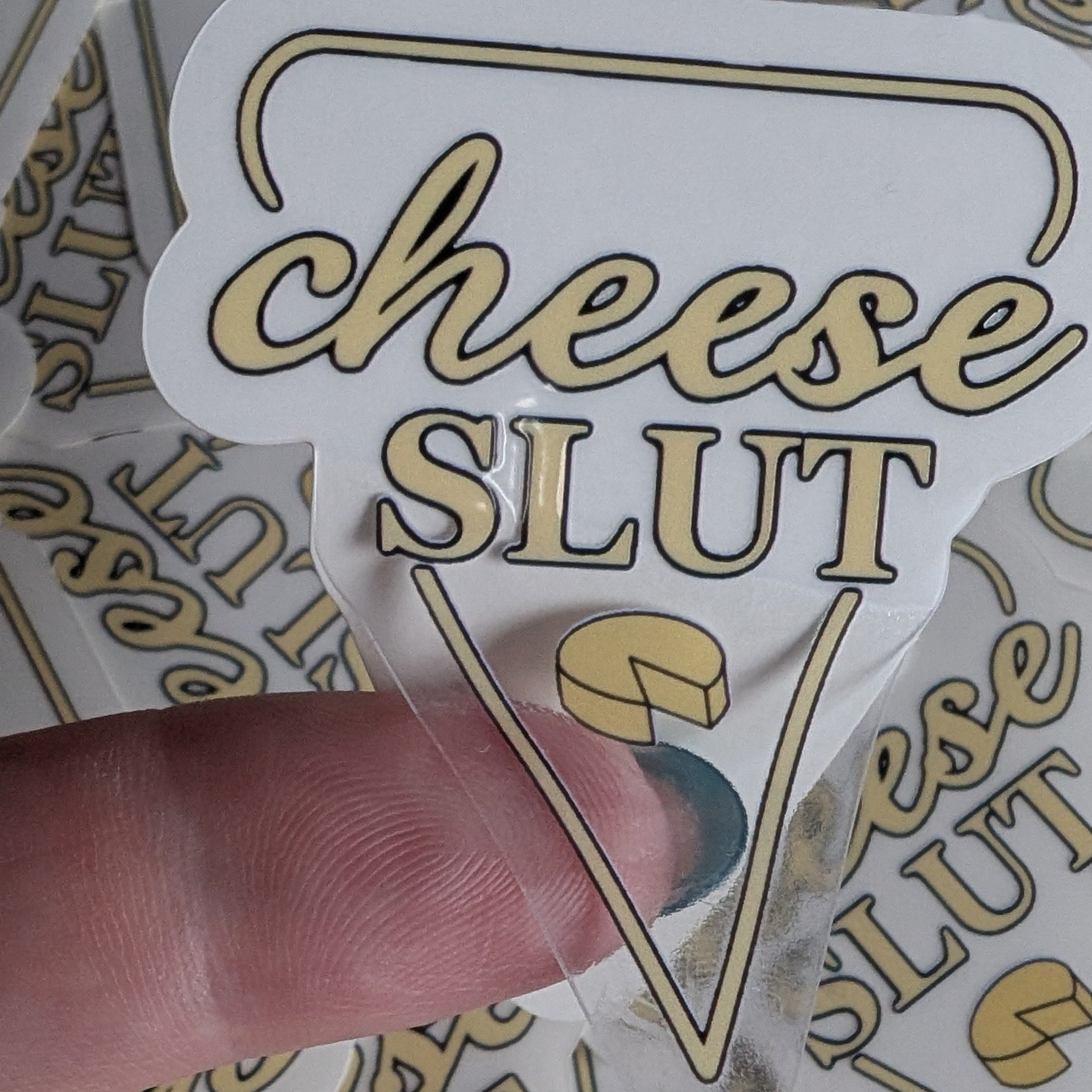 Sticker with 'cheese slut' text held by a finger over a background of similar stickers.