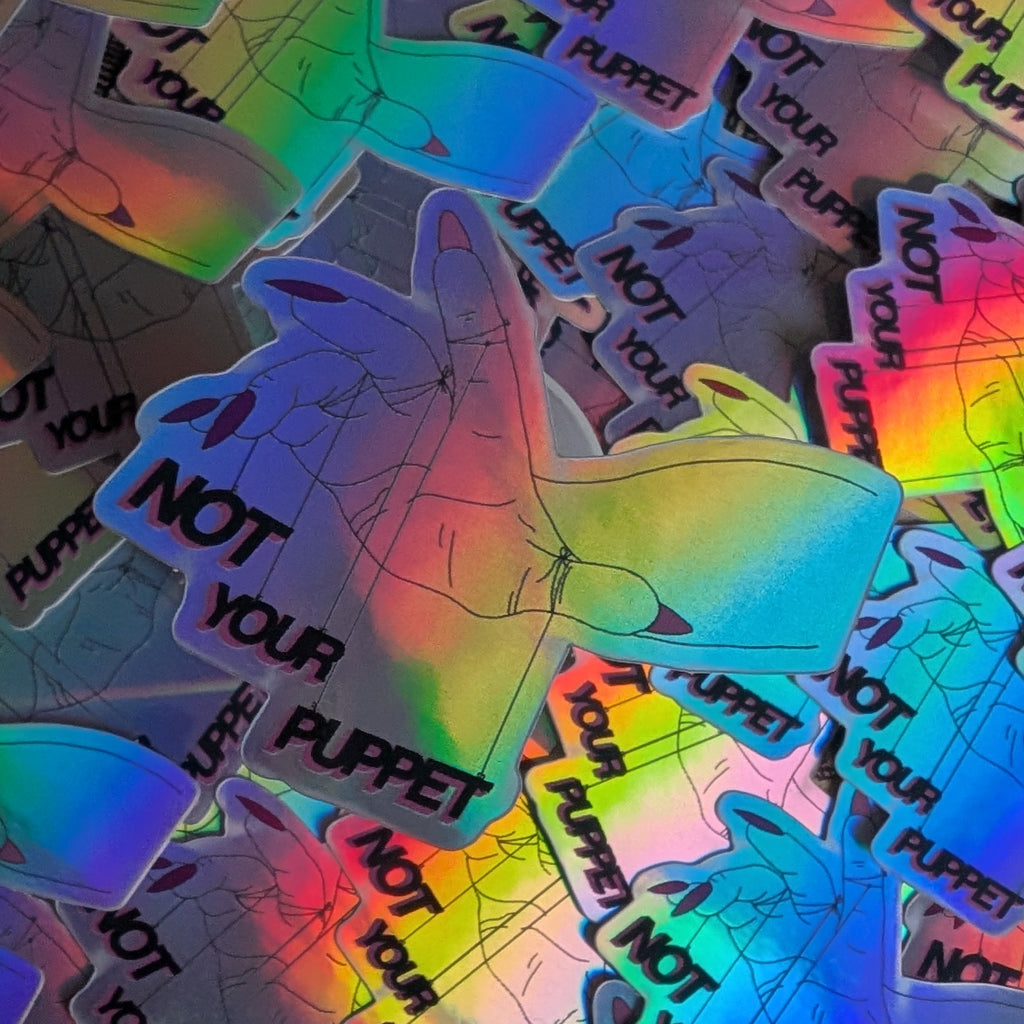 Holographic stickers with 'Not Your Puppet' text on a textured surface.