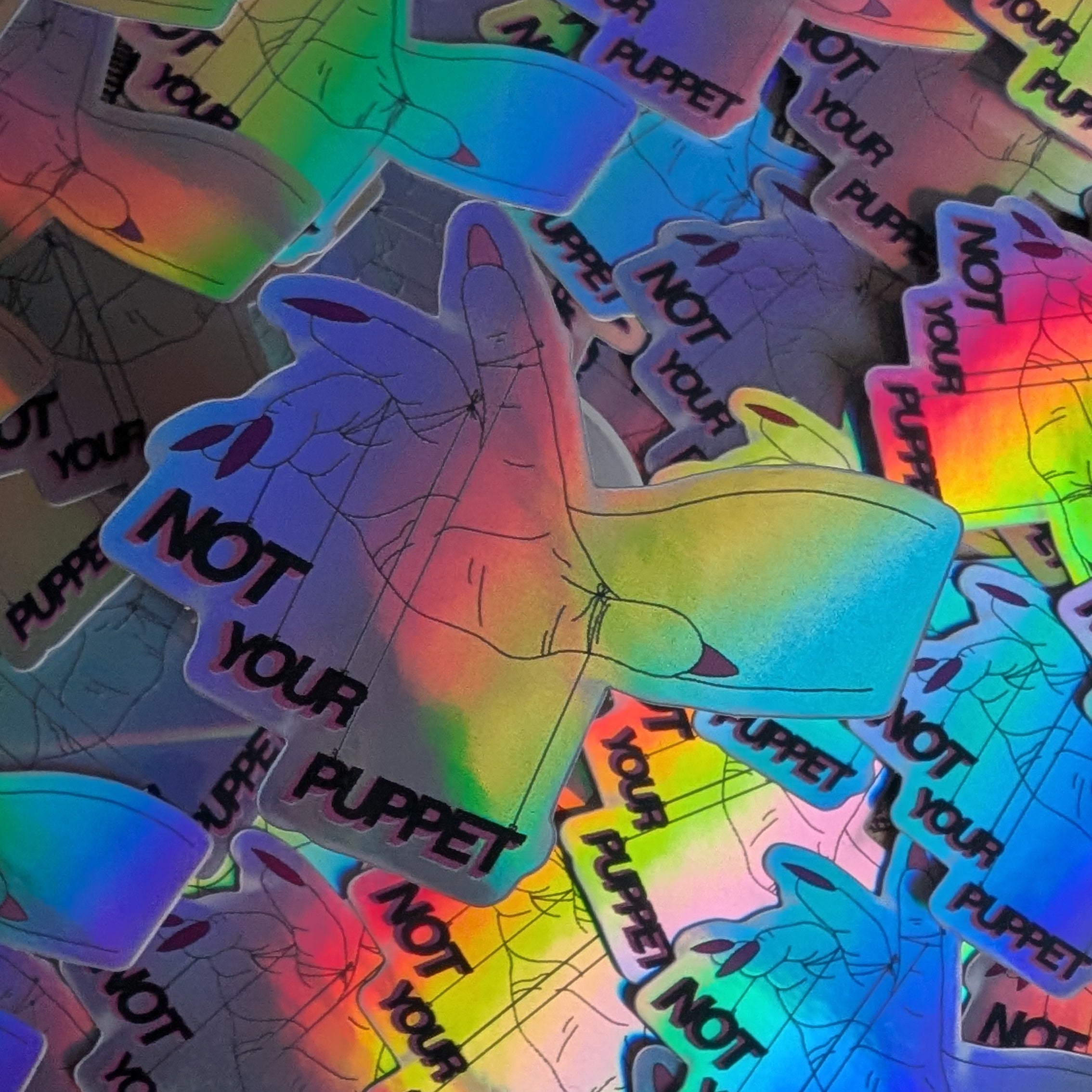 Holographic stickers with 'Not Your Puppet' text on a textured surface.