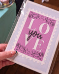 Card with 'LOVE you' text held by a hand on a wooden surface.