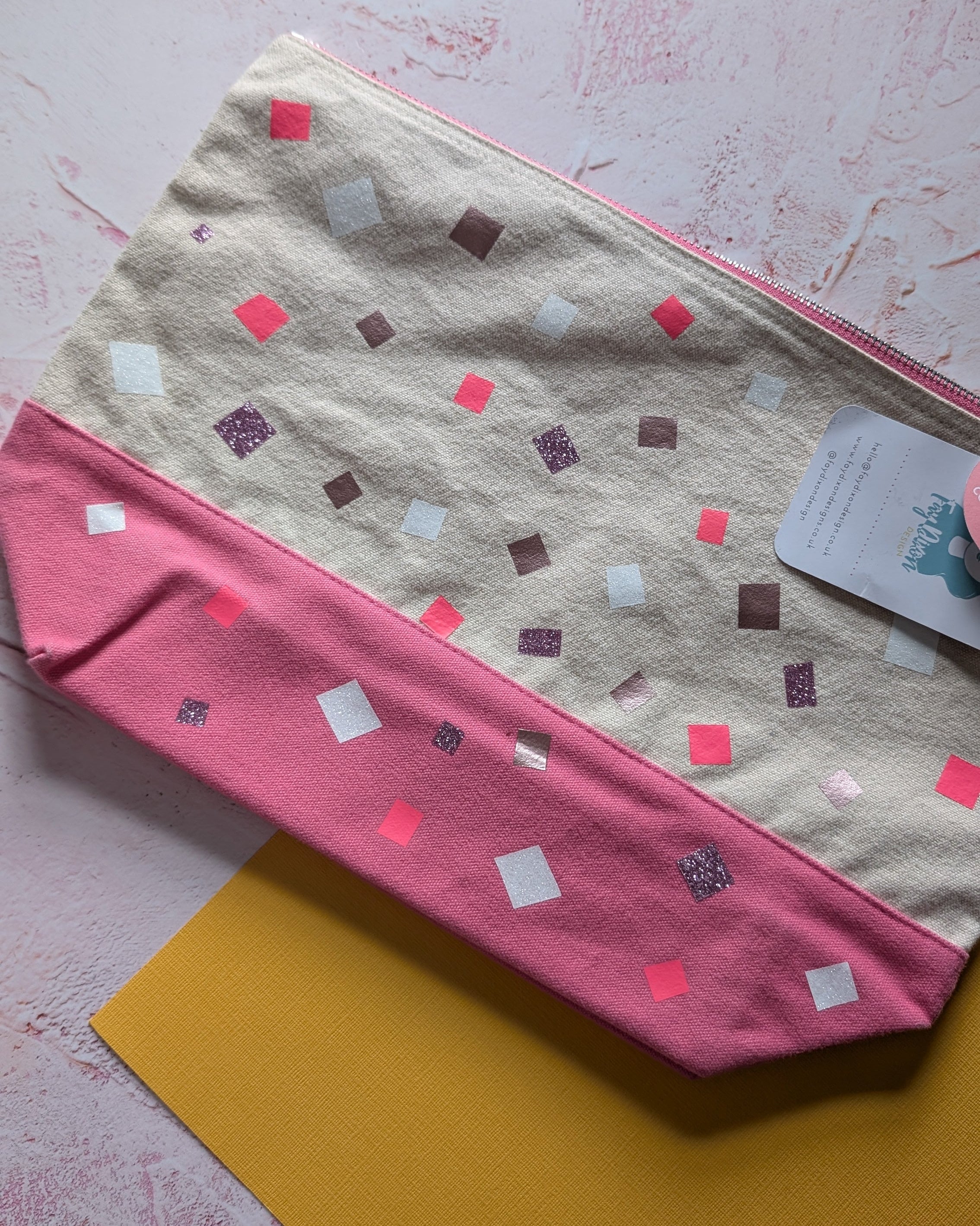 Two fabric swatches, one pink with square patterns and one beige, on a textured surface.