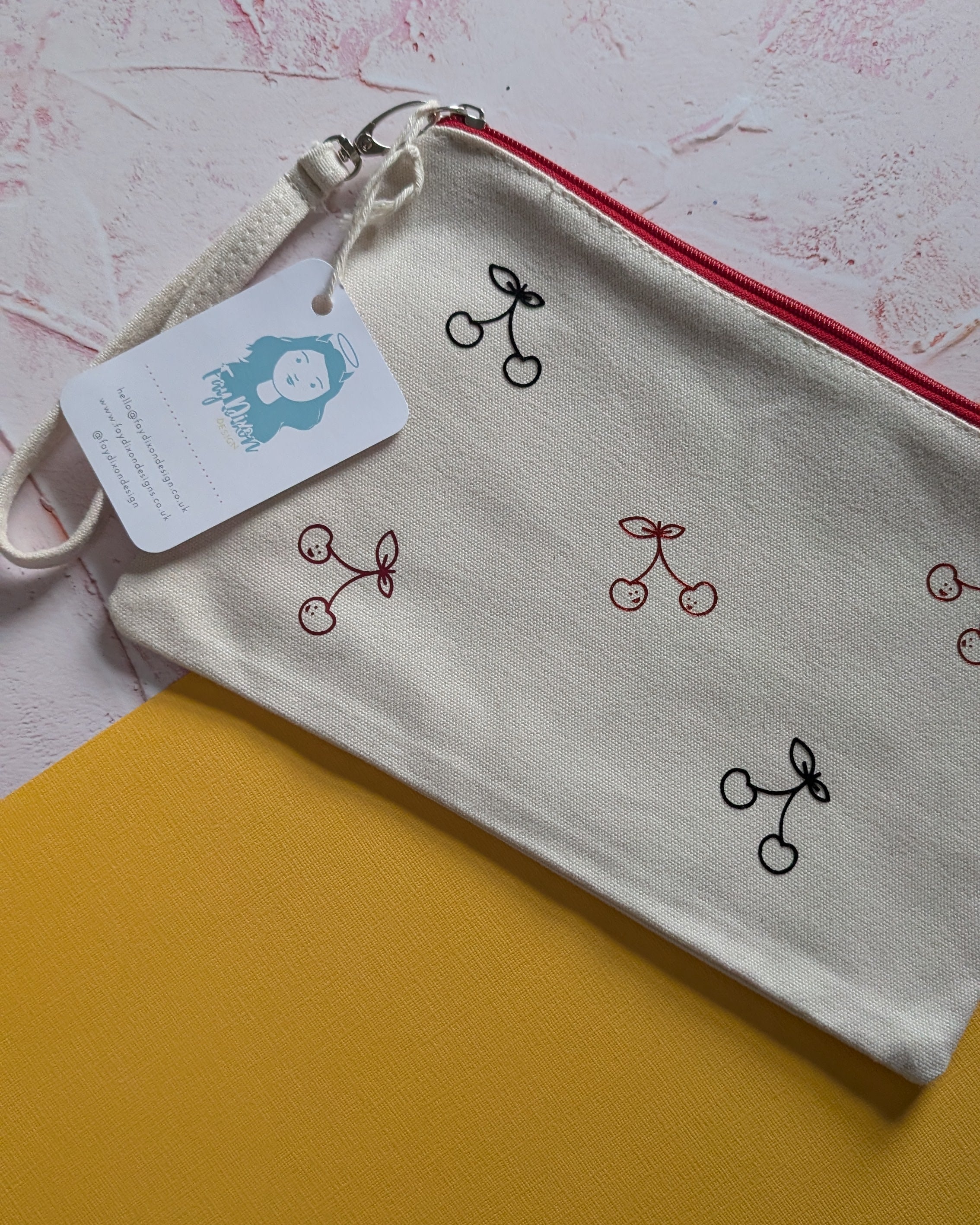 Small pouch with cherry design and tag on a textured surface