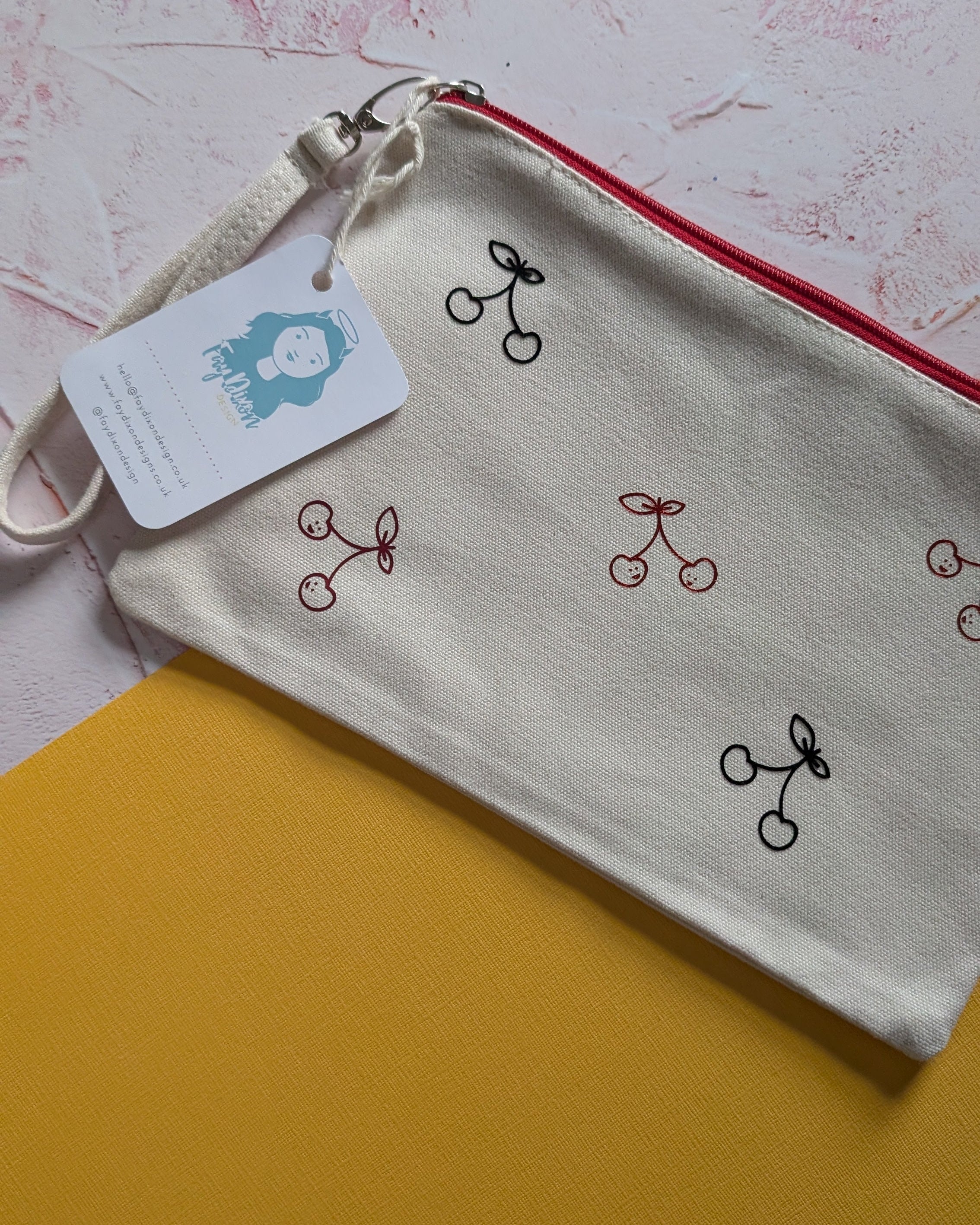 Small pouch with cherry design and tag on a textured surface