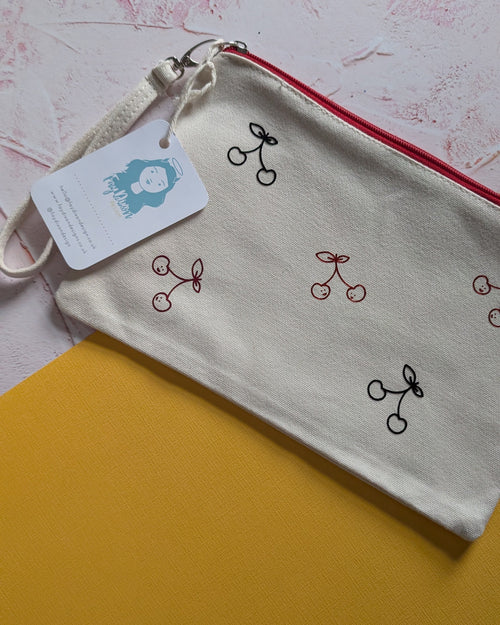 Small pouch with cherry design and tag on a textured surface